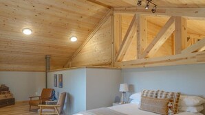 A bedroom with a wooden ceiling, a bed with white bedding, a chair, a nightstand, and a lamp.