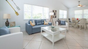 Un salon avec un canapé bleu, une table basse blanche et un coin repas comprenant une table et des chaises.