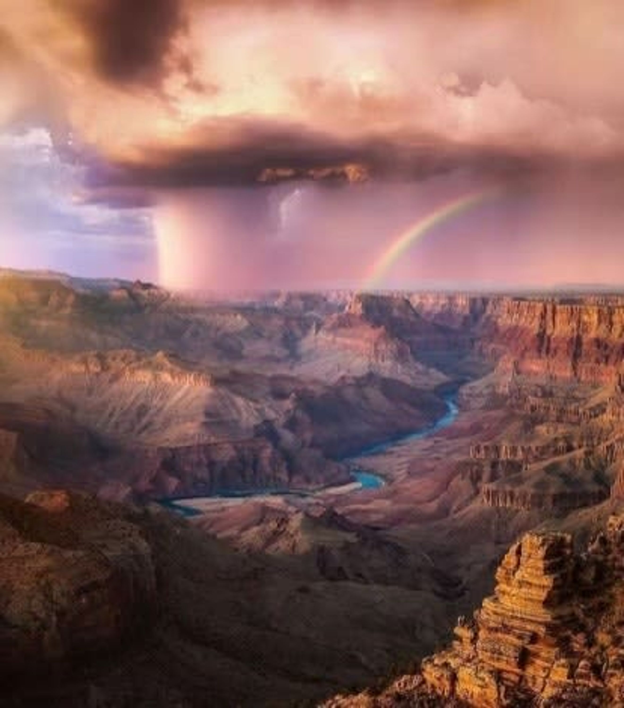 Un canyon avec une rivière, un arc-en-ciel et un ciel orageux.