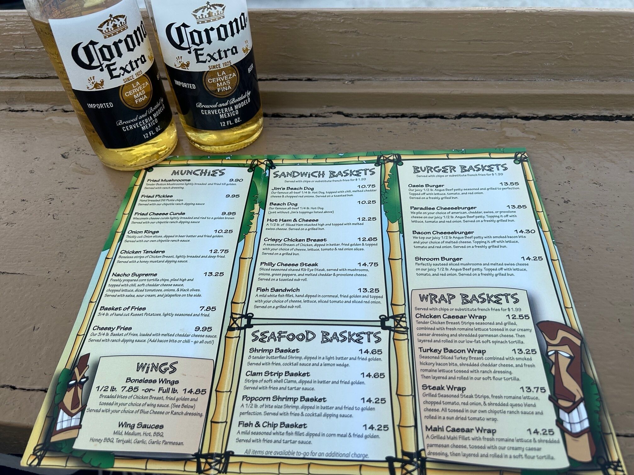 Un quadre de menú amb diferents plats i preus, i dues ampolles de Corona Extra.