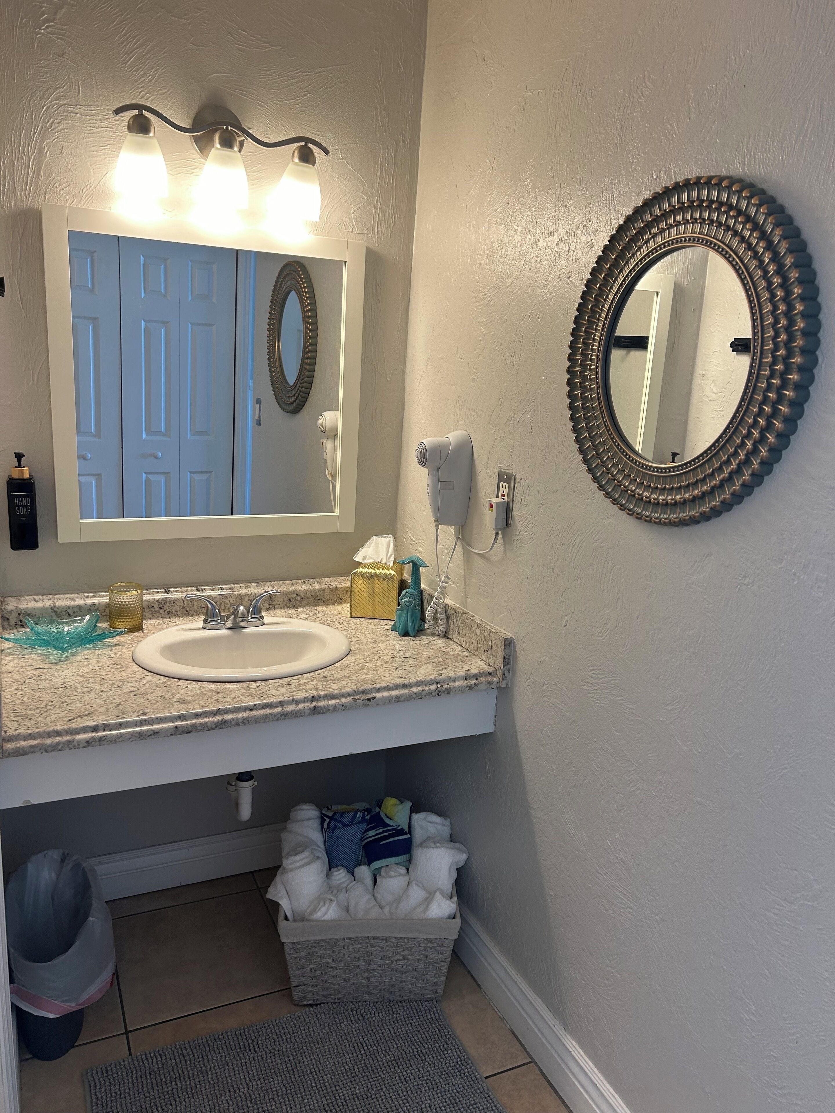 A bathroom with a white sink, a mirror, a hair dryer, and a basket of towels.