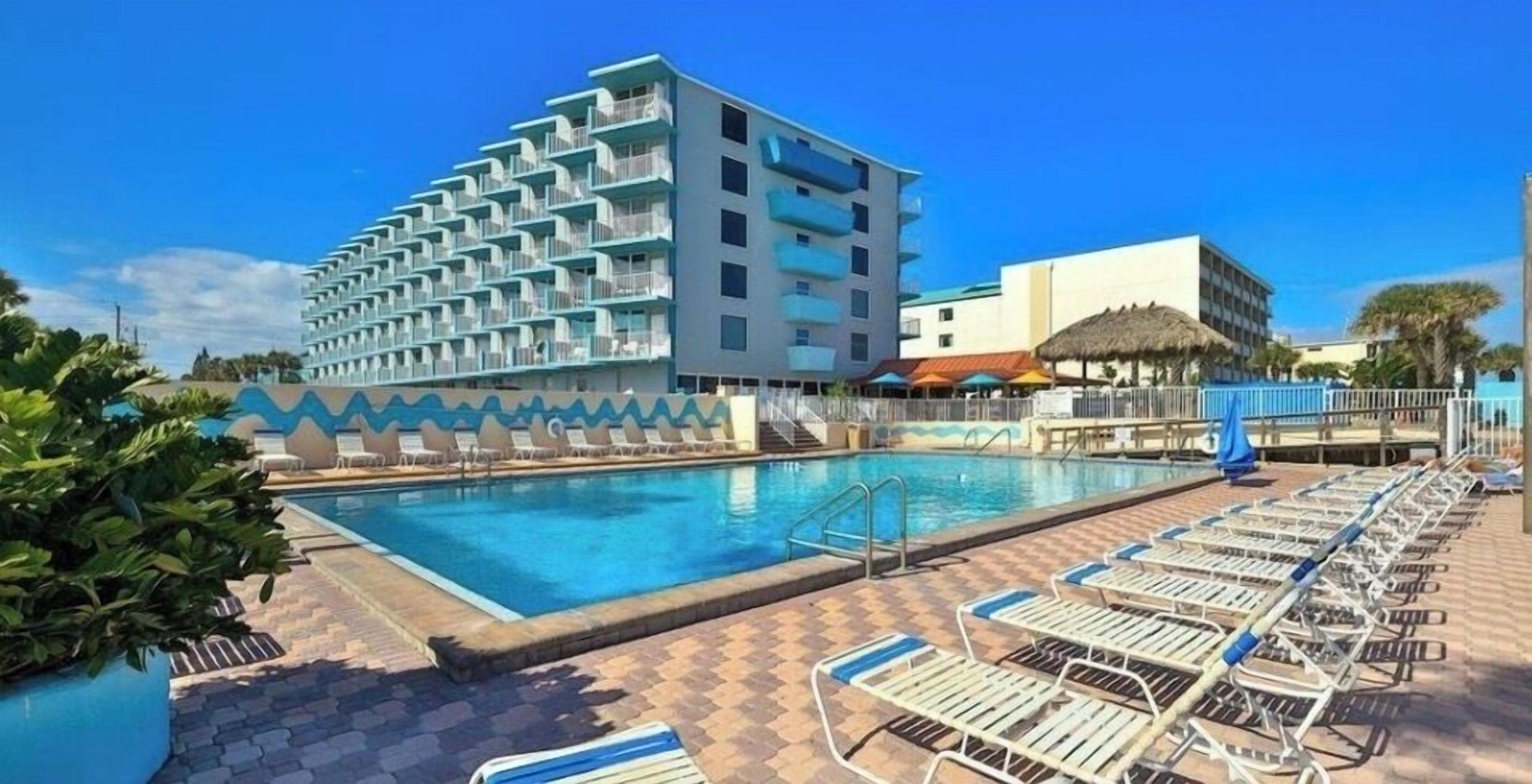 A hotel with a swimming pool, lounge chairs, and a building with multiple balconies.