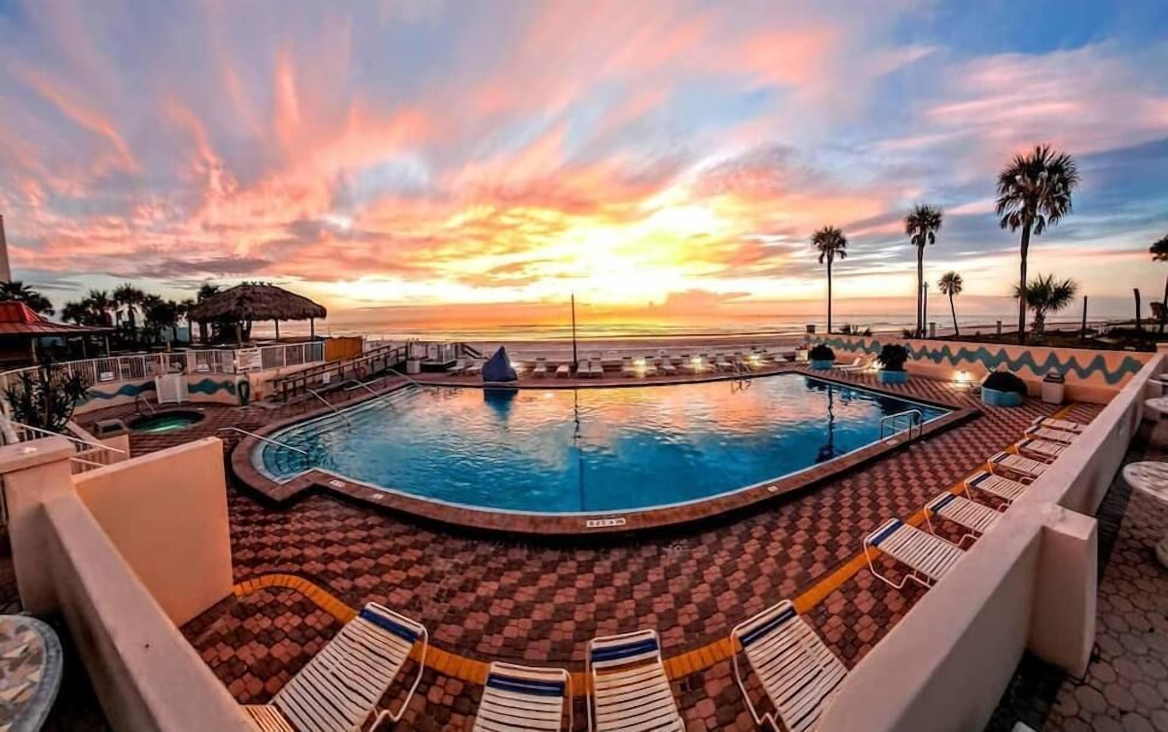 Ein Poolbereich mit Liegestühlen und Blick auf den Sonnenuntergang über dem Meer.
