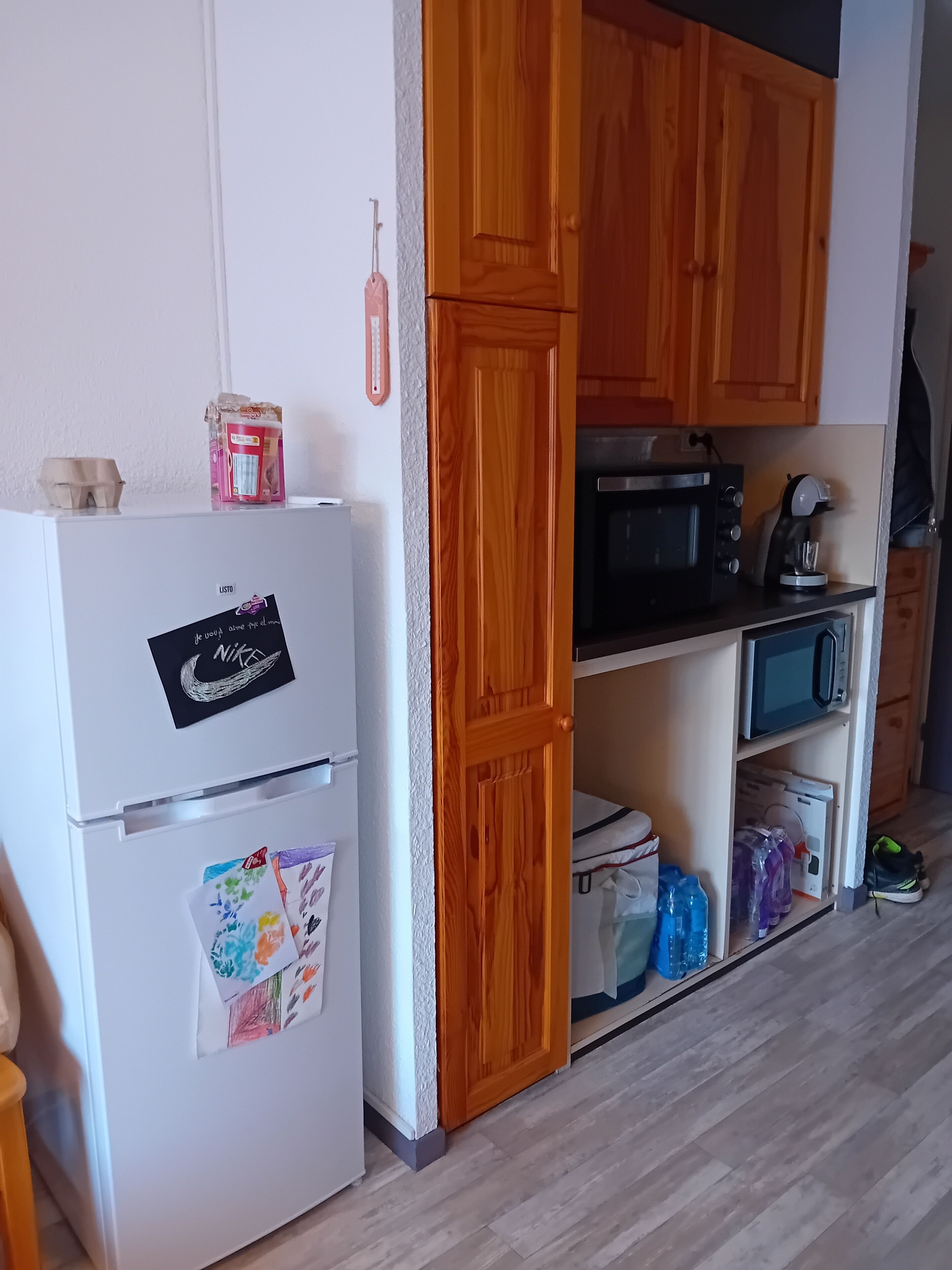 A compact kitchen with wooden cabinets, a white refrigerator, a microwave, and a coffee maker.