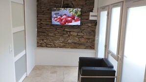 A room with a stone wall, a television mounted on it, and a black bench.