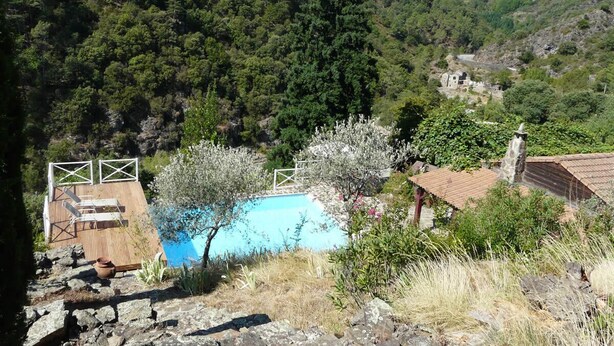 A pool area with a wooden deck, a stone wall, and a view of a forested valley.
