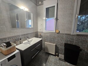 A modern bathroom with a large mirror, a white sink, a black vanity, a radiator, and a black trash bin.