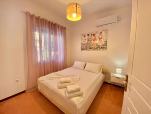 A bedroom with a bed, curtains, a painting, and a bedside lamp.