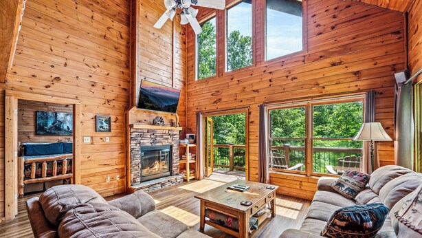 A cozy cabin interior with a fireplace, wooden walls, large windows, and a comfortable seating area. - Hot tub|Fireplace|FastWiFi|Convenient|Pet Friendly (Pigeon Forge)