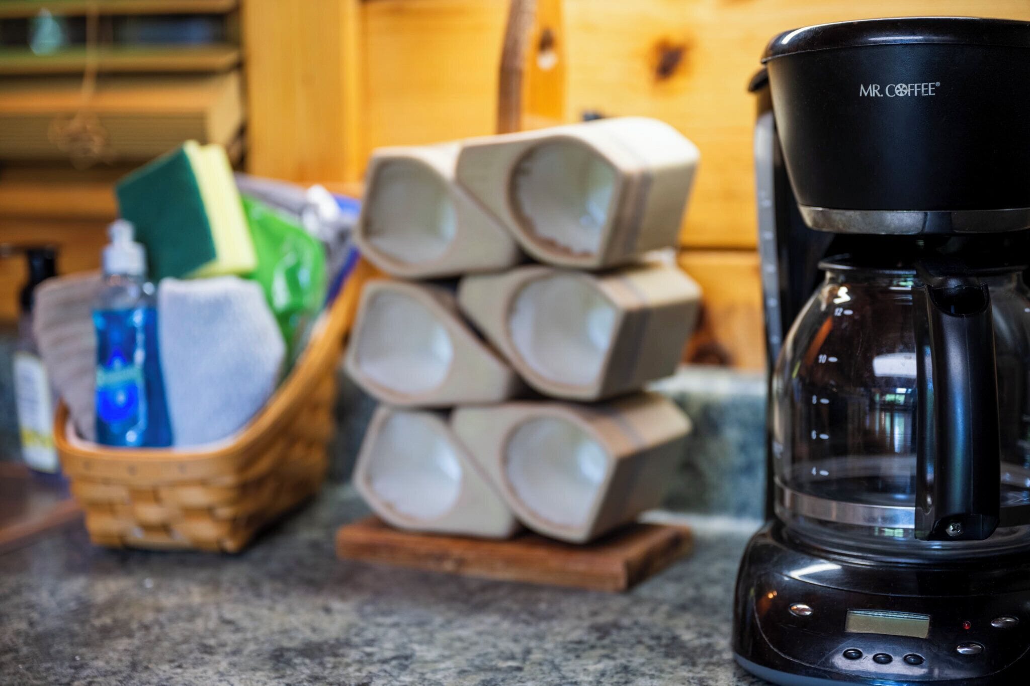 Une machine à café dotée d’un écran numérique, une pile de tasses en céramique et un panier contenant des produits de nettoyage, le tout posé sur un plan de travail de cuisine.
