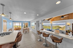 A modern kitchen with a large island, bar stools, and a view of the beach. - Lands End - Ocean Front w/Beach Path & Spa (Gold Beach)