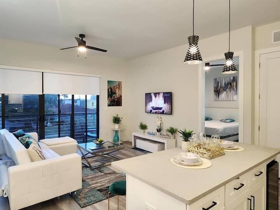 Una sala de estar moderna con un sofá, una mesa de centro y un televisor. Hay una zona de cocina con una mesa de comedor y sillas.