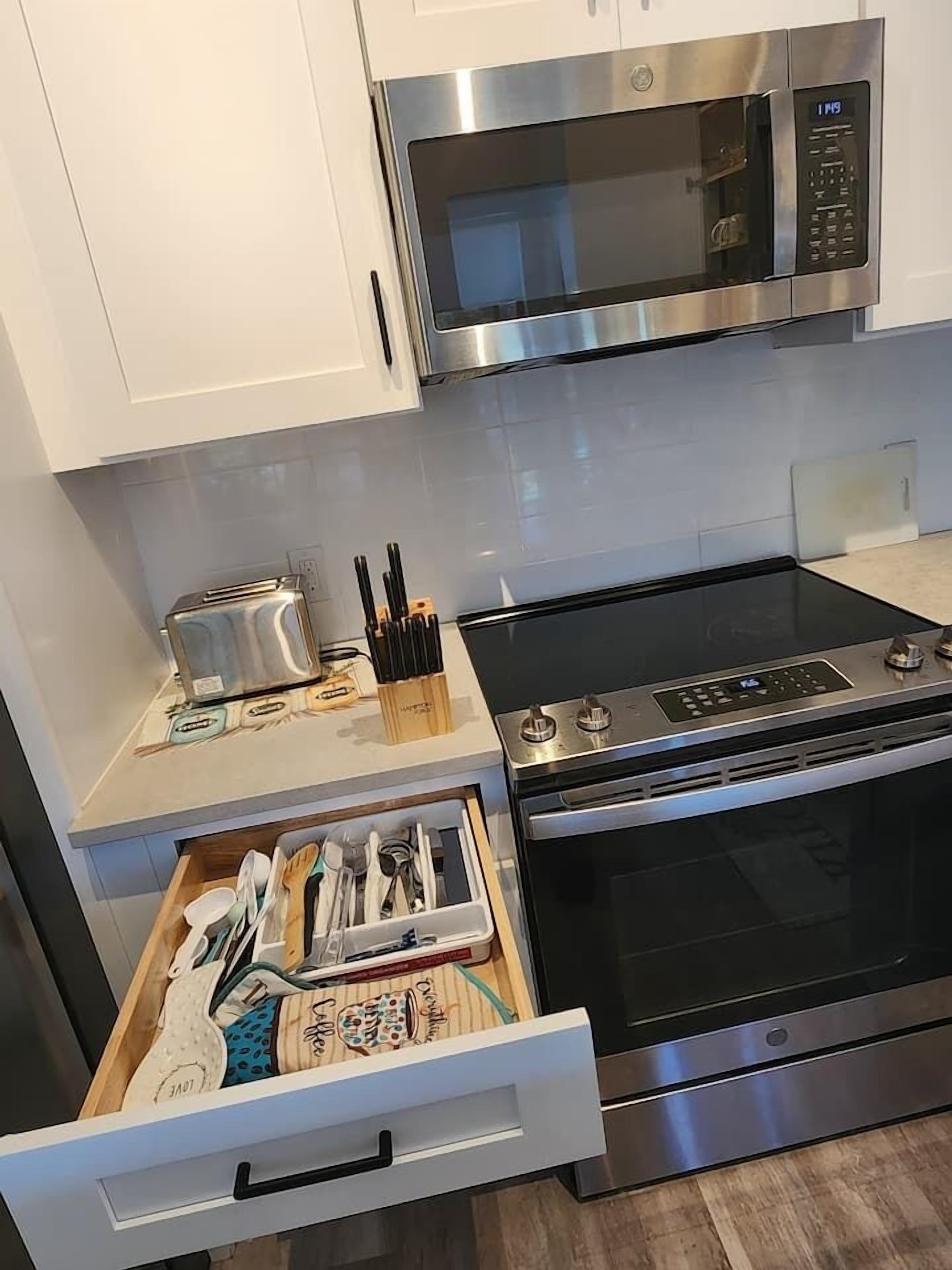 A kitchen with a stainless steel microwave, a toaster, and a drawer organizer with utensils.