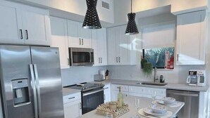 A modern kitchen with white cabinets, stainless steel appliances, and a central island set for dining. - Lux place  green Cozy 3 Beds 2rooms (West Palm Beach)