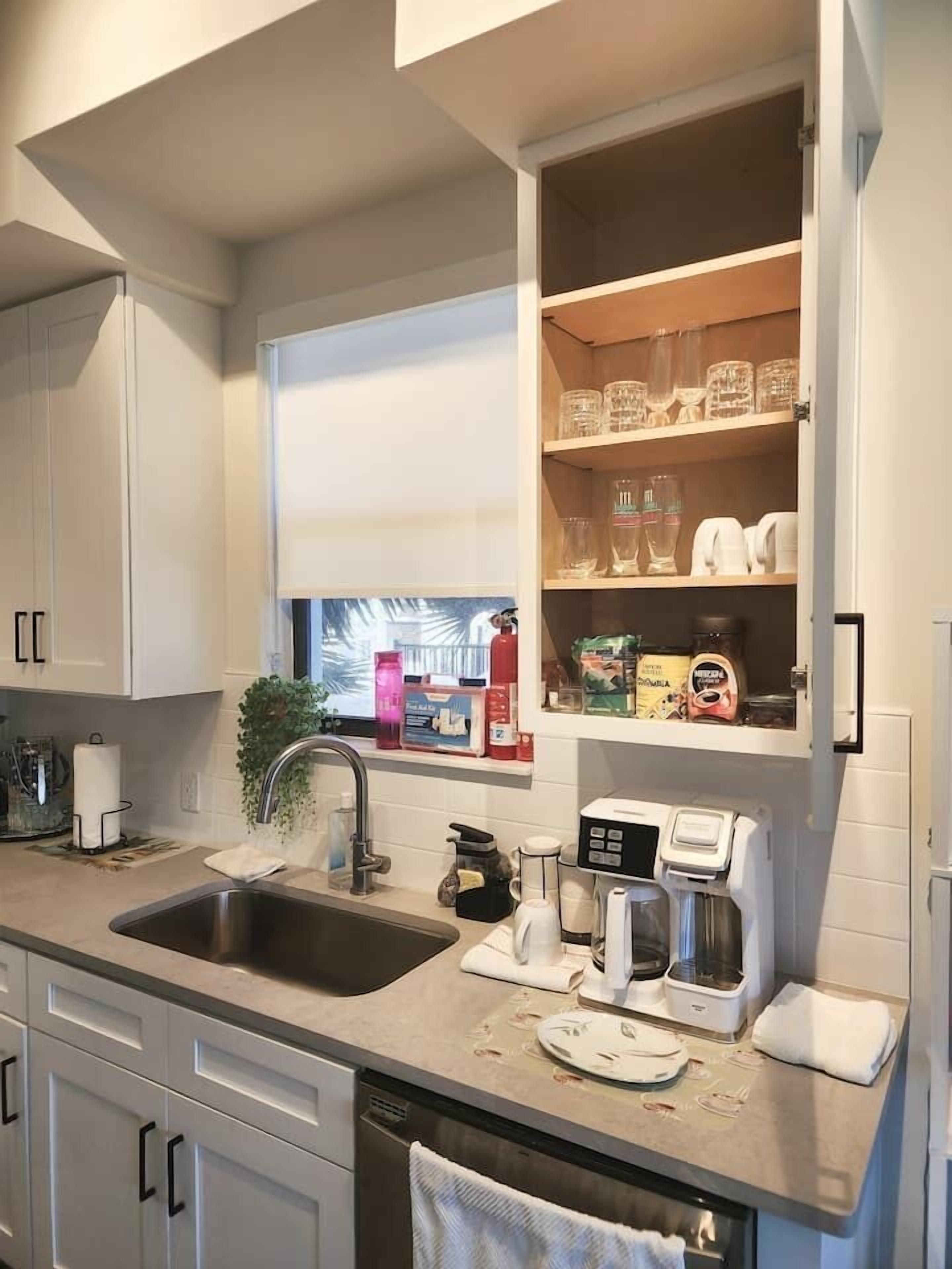 Una cocina moderna con armarios blancos, un ventanal integrado y una cafetera.