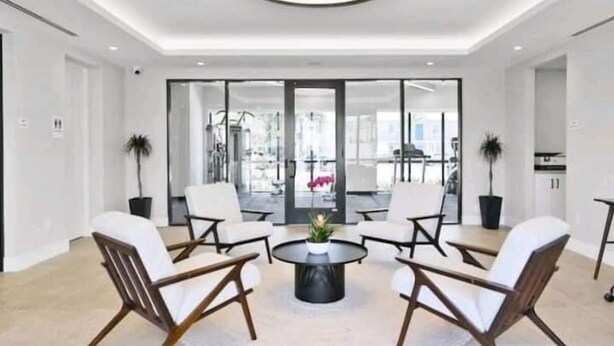 A modern interior with a round coffee table surrounded by white chairs, a large window, and a view of the outdoors. - Lux place  green Cozy 3 Beds 2rooms (West Palm Beach)