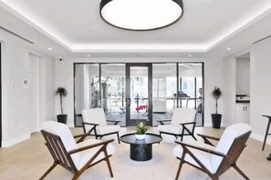 A modern interior with a round coffee table surrounded by white chairs, a large window, and a view of the outdoors.