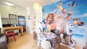 Comedor con una mesa preparada para dos, un taburete rojo y un mural de personajes animados.