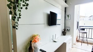 Una sala de estar moderna con una consola blanca, un televisor de pantalla plana montado, un jarrón con flores y una planta en maceta.