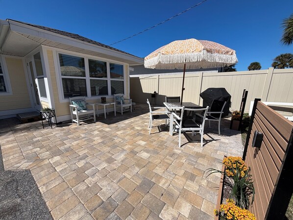 A patio area with a table and chairs, a covered grill, and a large umbrella.