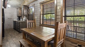 A wooden interior with a dining table and chairs, wooden cabinets, and a window with blinds. - Peaceful Family Lake House near SDC Walk to Lake (Branson)