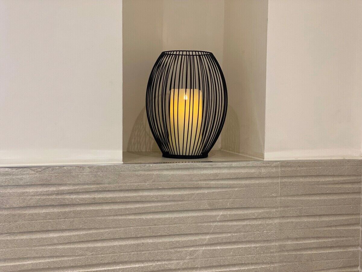 Een moderne, getextureerde muur met een cilindrisch, zwart, draadframeobject in het midden van een plank.
