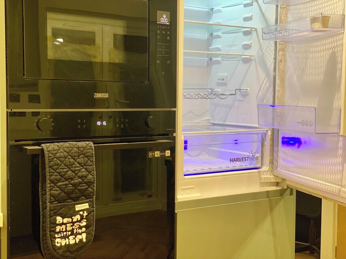 A kitchen with a black microwave, oven, and a white refrigerator with a blue light.