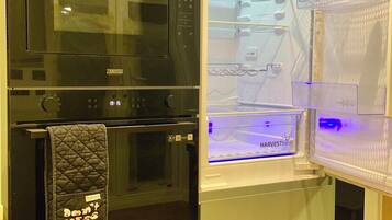 A kitchen with a black microwave, oven, and a white refrigerator with a blue light.