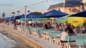 Ein Restaurant direkt am Strand mit Außenplätzen, Sonnenschirmen und Blick auf das Wasser.