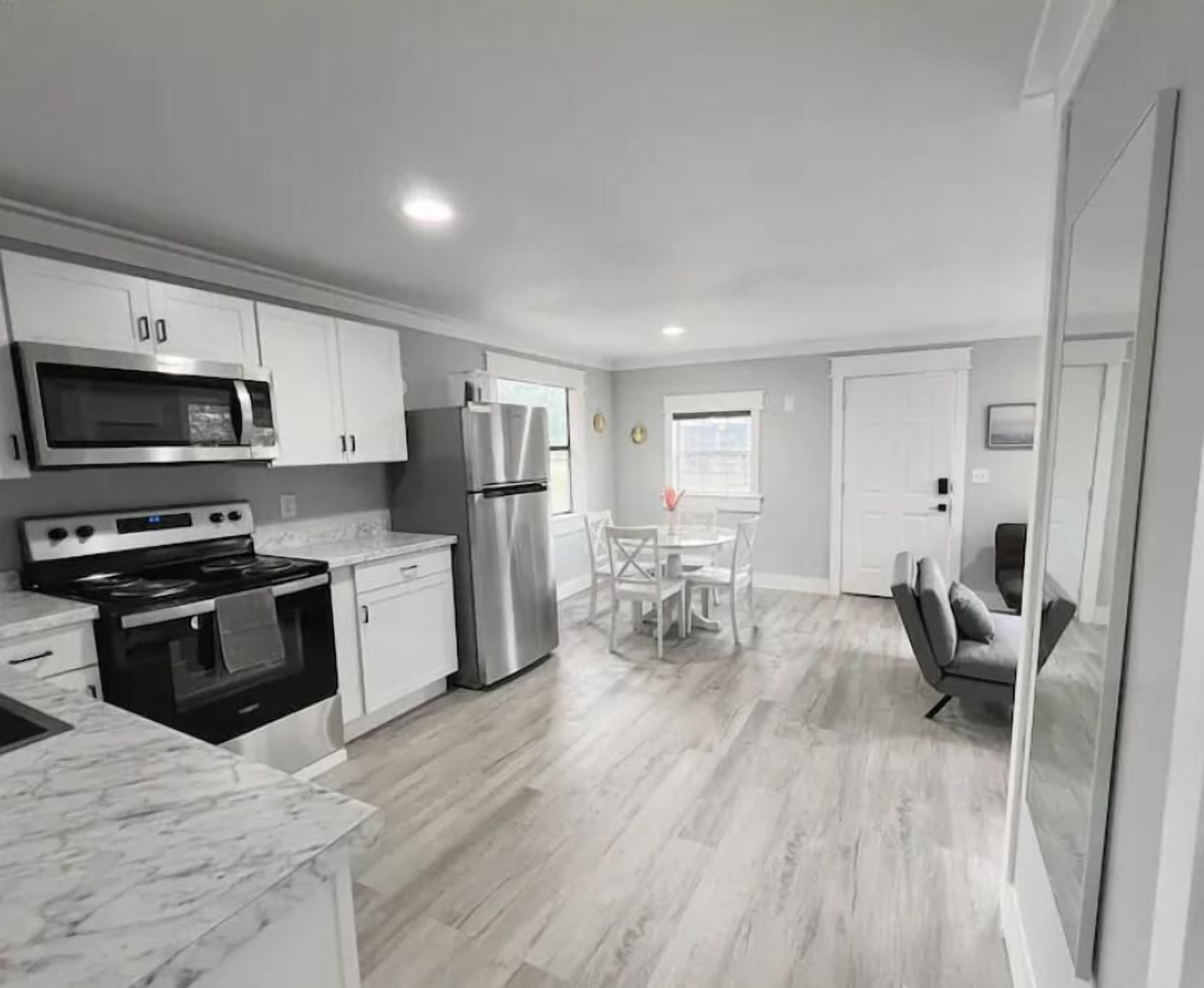 Una cocina moderna con armarios blancos, electrodomésticos de acero inoxidable y un comedor con mesa y sillas blancas.