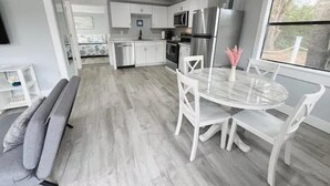 Eine moderne Küche mit weißen Schränken, Edelstahlgeräten und einem Essbereich mit einem Marmortisch und weißen Stühlen.