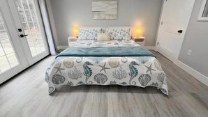 Ein Schlafzimmer mit einem Bett, zwei Nachttischen, einer Kommode, einer Tür und einem Wandbild.