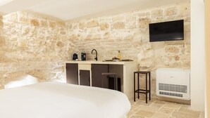 A bedroom with a stone wall, a bed, a small kitchenette with a sink and a flat-screen TV mounted above it. - SUITE LE GROTTE - suite with heated pool and whirlpool (Ostuni)