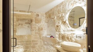A bathroom with a stone wall, a round mirror, a sink, and a shower area. - SUITE LE GROTTE - suite with heated pool and whirlpool (Ostuni)