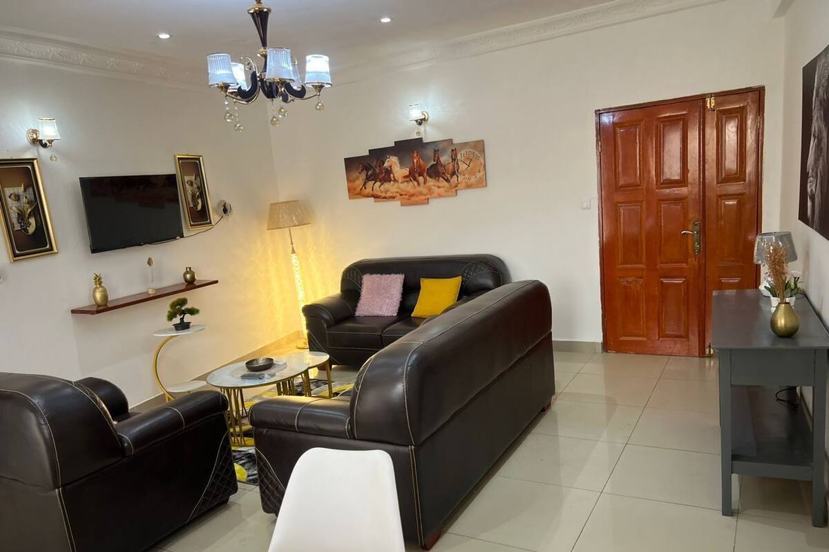 Una sala de estar con un sofá de cuero negro, un sillón blanco, una mesita redonda y un televisor montado en la pared.