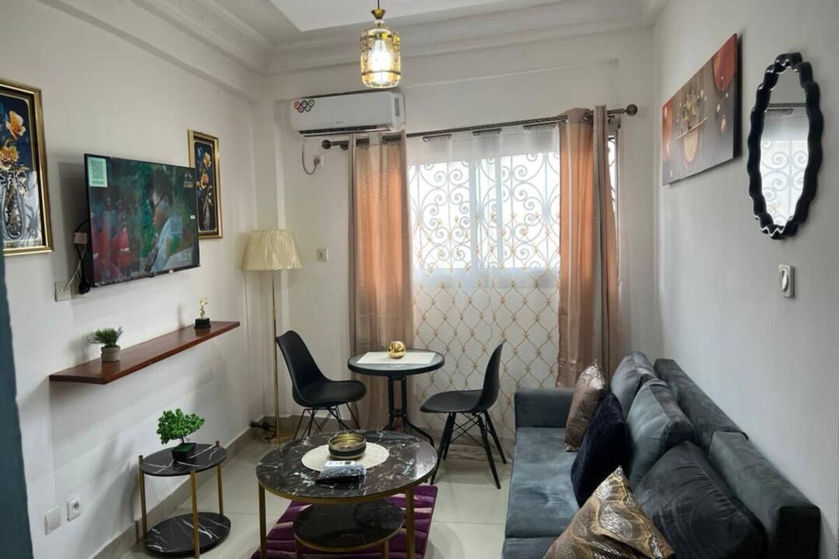 Una sala de estar con sofá, una mesa de centro, televisor y un comedor con sillas y una mesa pequeña.