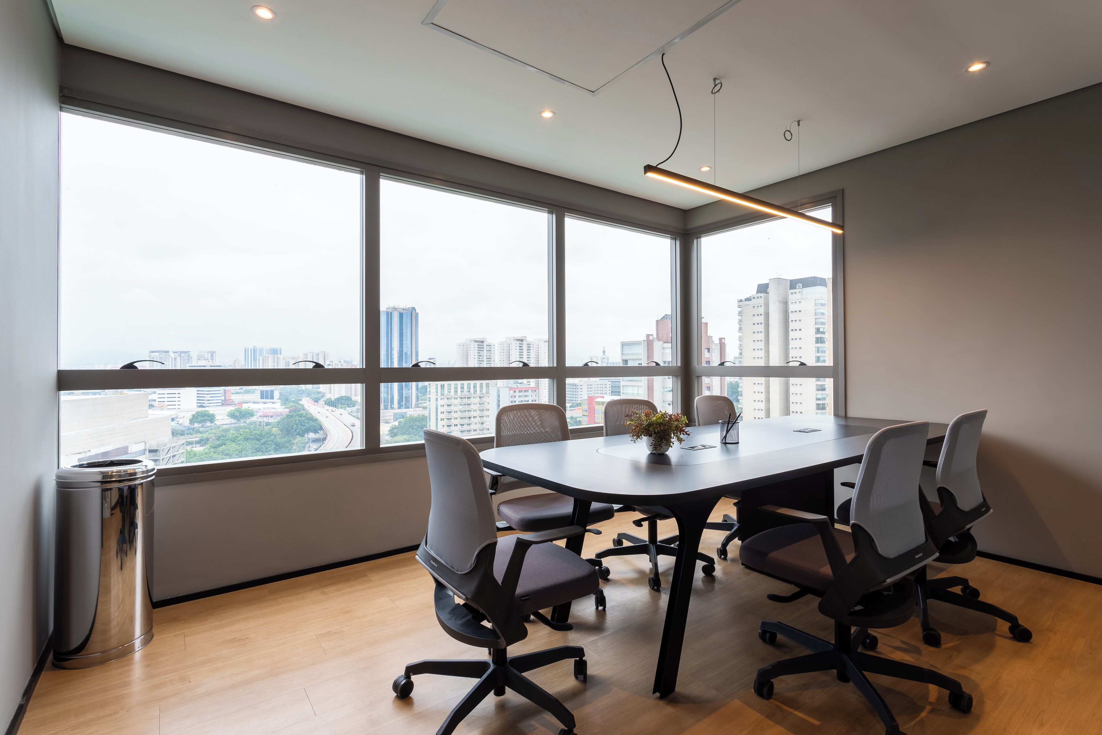 A conference room with a large table, six chairs, and a view of a cityscape through large windows.
