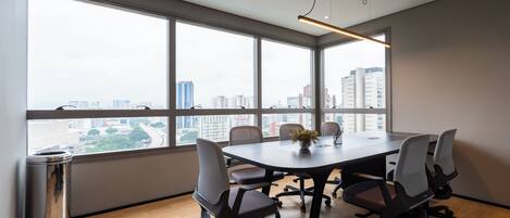 A conference room with a large table, six chairs, and a view of a cityscape through large windows.
