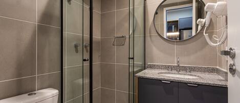 Une salle de bain moderne dotée d’une douche à parois de verre, de toilettes, d’un lavabo avec un plan de travail en granit et d’un sèche-cheveux fixé au mur.
