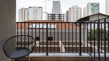 A balcony with a black chair, a view of a cityscape with tall buildings, and a tiled roof.