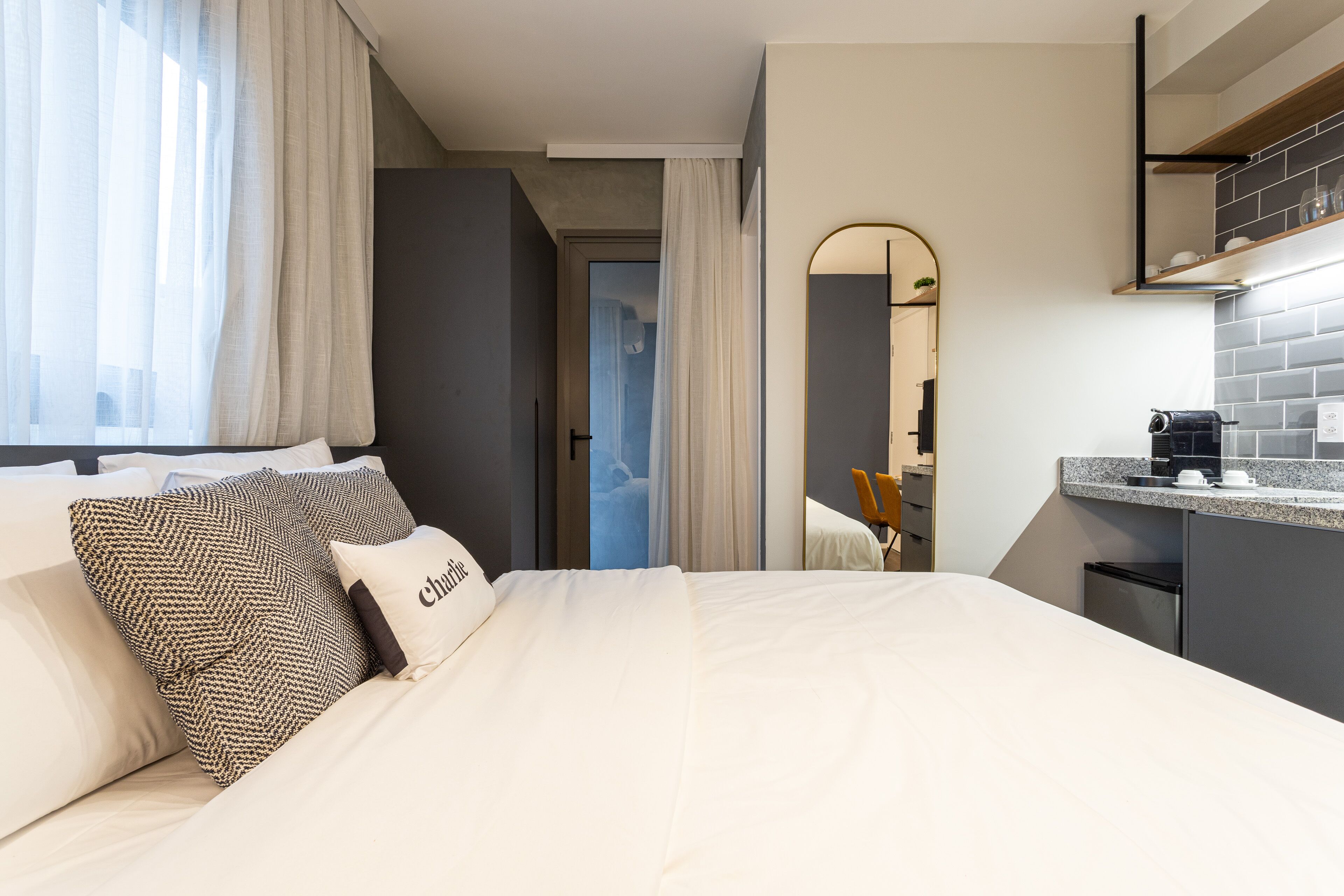 Een moderne hotelkamer met een groot bed, een kleine kitchenette en een zichtbare badkamer achter een deur.