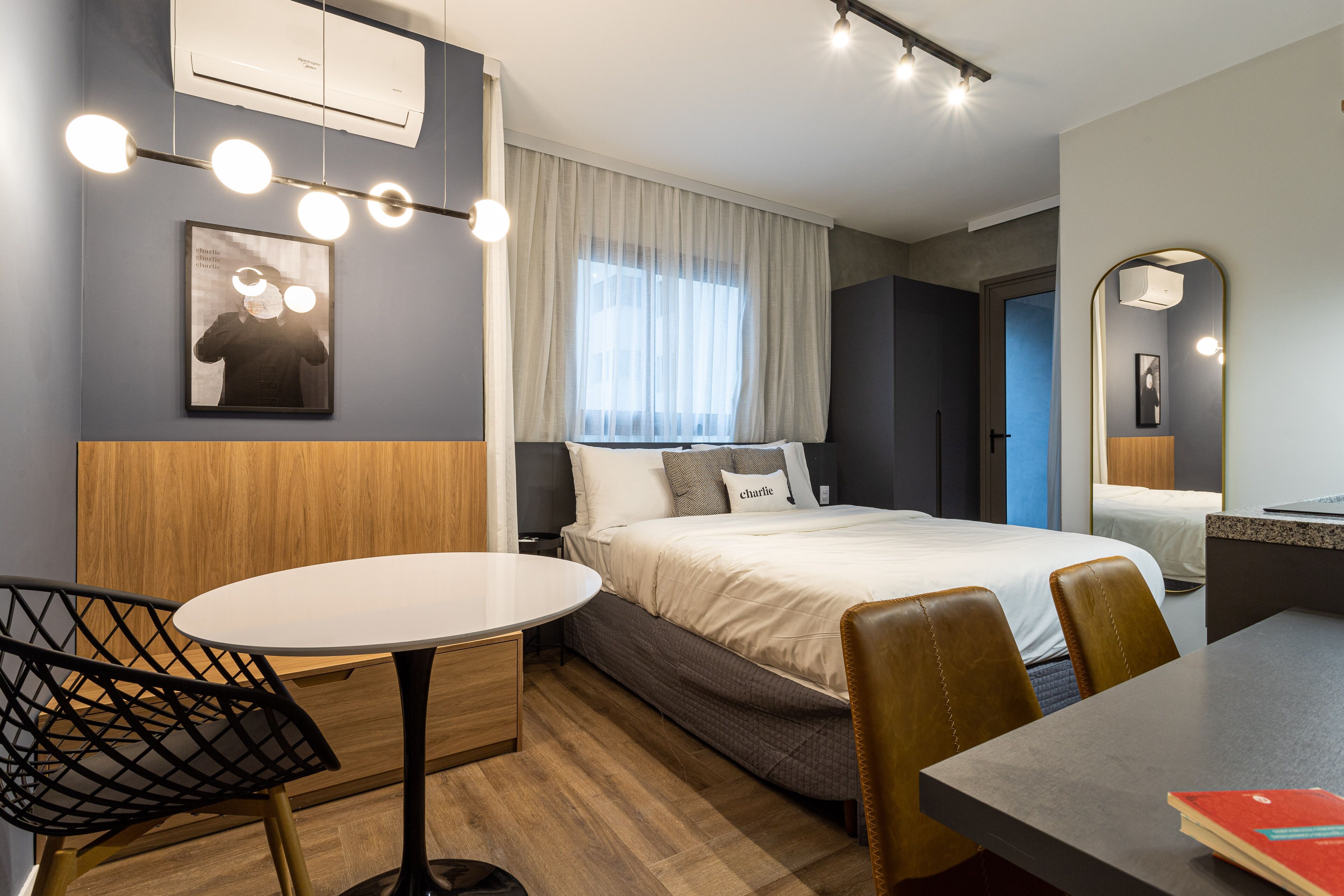 Een hotelkamer met een bed, een ronde tafel, twee stoelen, een bijzettafeltje, een spiegel en een schilderij aan de muur.