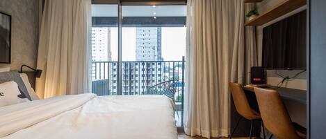 Una habitación de hotel moderna con una cama grande, un escritorio con dos sillas, un televisor y un balcón con cortinas.
