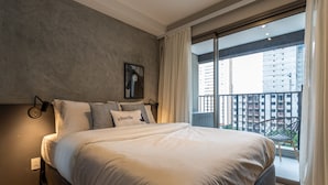 Habitación de hotel moderna con una cama grande, vista de la ciudad desde un balcón y un cuadro en la pared.