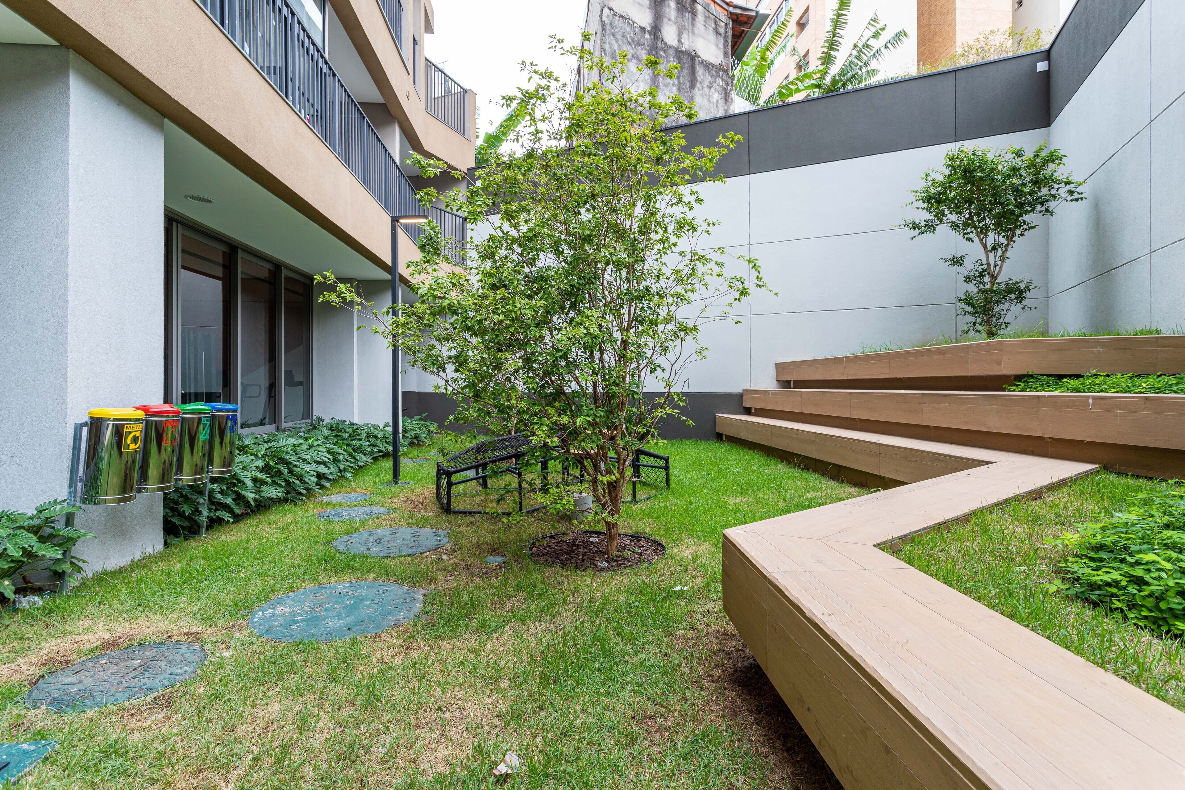 A courtyard with a small tree, a wooden bench, and a trash bin.