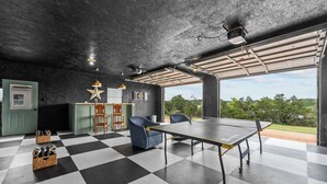 A room with a ping pong table, checkered floor, and a view through a large window. - The ultimate retreat! Enjoy our hot tub, game room, and serene deer sightings. (Fredericksburg)
