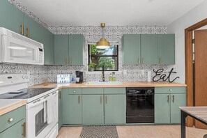 Een keuken met groene kastjes, een witte magnetron, een koffiezetapparaat en een spoelbak.