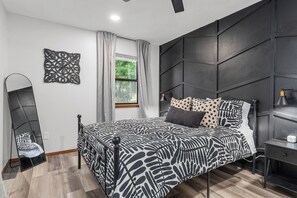 Een moderne slaapkamer met een bed, nachtkastje, spiegel en raam met gordijnen.