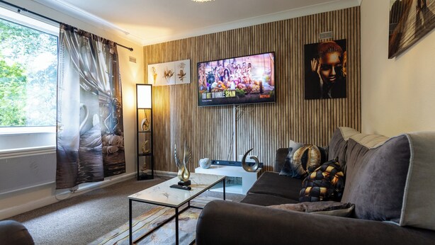 Een woonkamer met een flatscreen televisie, een bank, een salontafel en een raam met gordijnen.