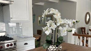 Una cocina con armarios blancos, una isla de madera con un cuenco decorativo y orquídeas blancas.